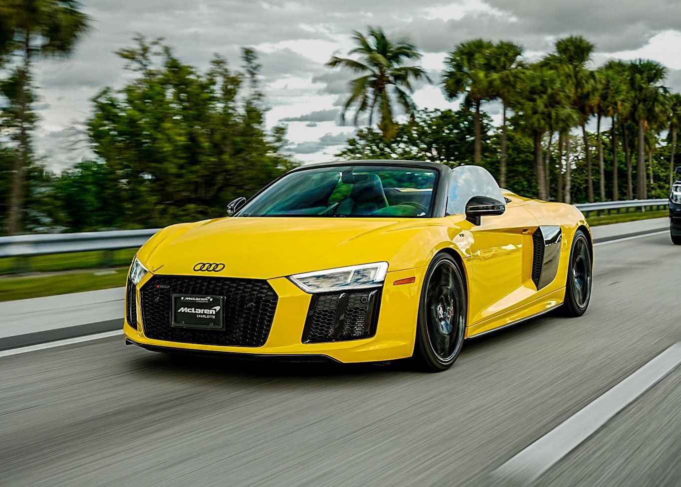 A yellow Audi R8 convertible is driving down a highway.