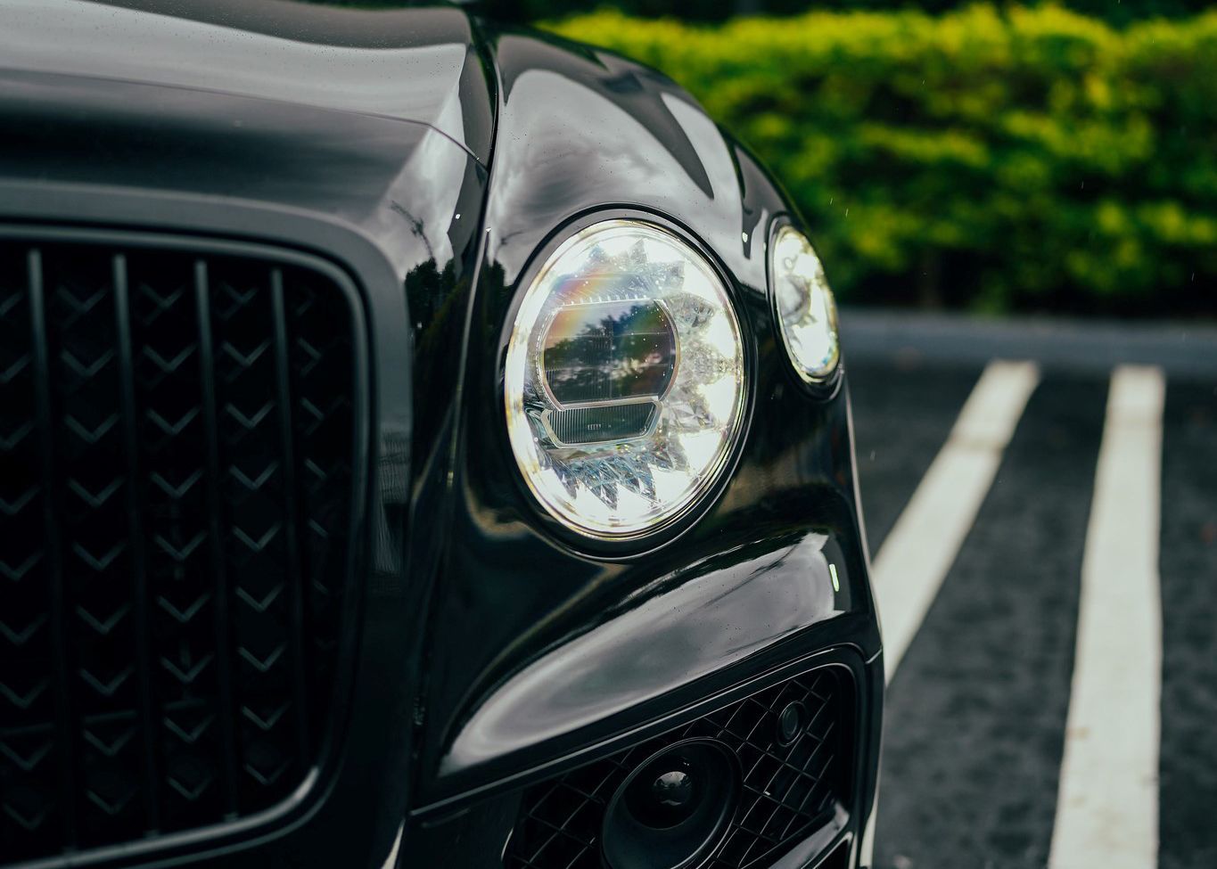 A close up of a black car 's headlight in a parking lot.