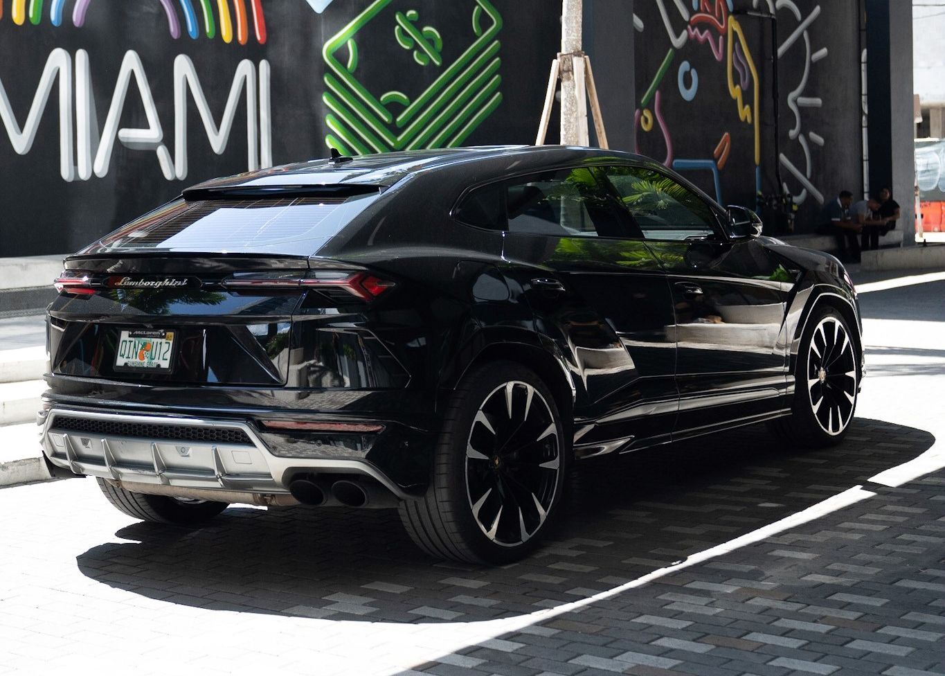 A black Lamborghini Urus is parked in front of a Miami wall.