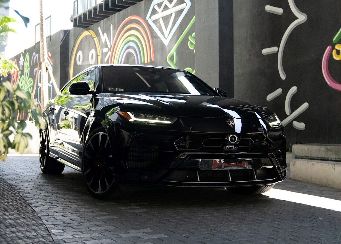 A black car is parked in front of a wall with graffiti on it.