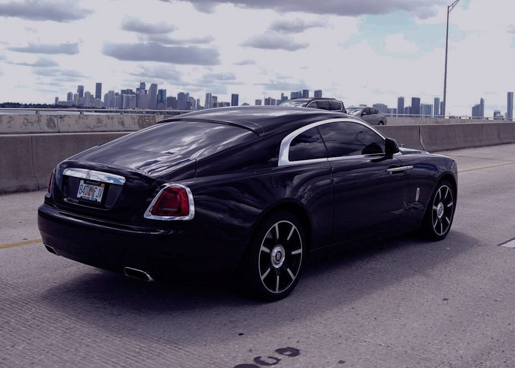 A black car is parked on the side of a highway in front of a city skyline.