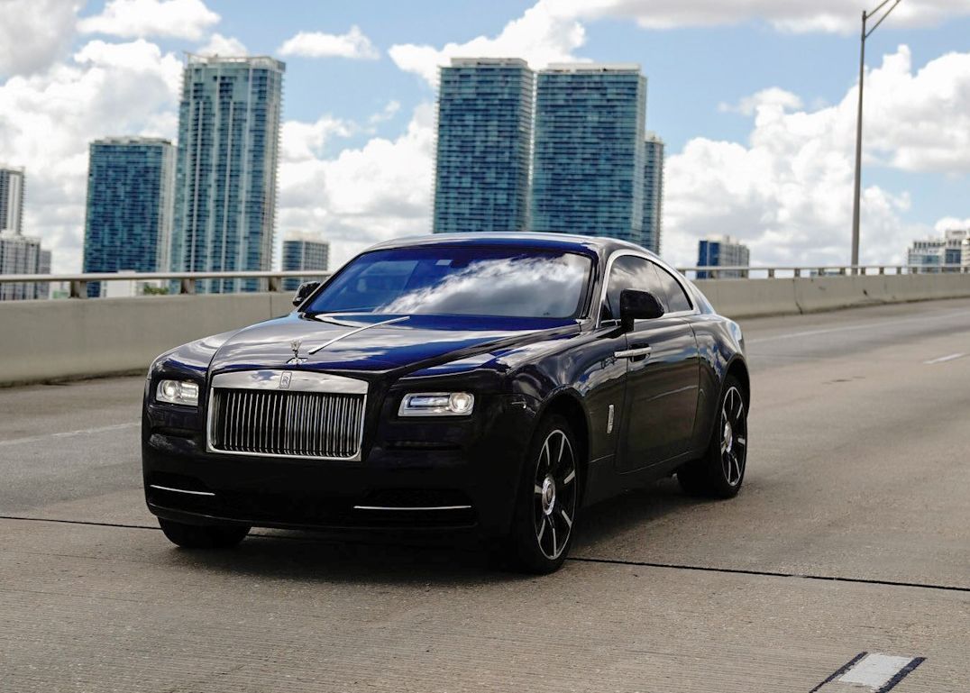 A black car is driving down a highway in front of a city skyline.