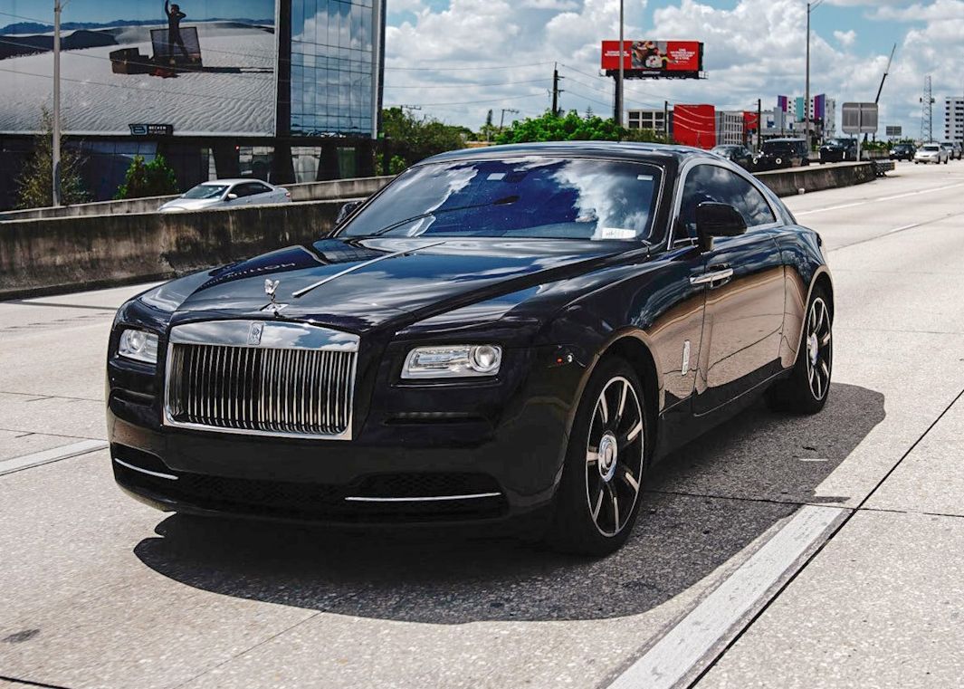 A black Rolls Royce is parked on the side of a highway.