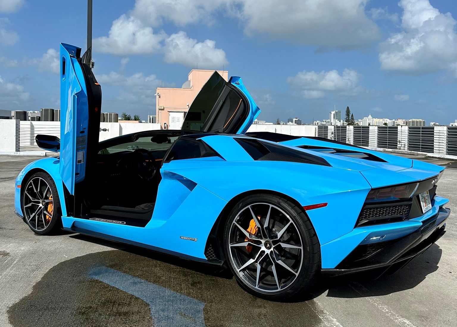 A blue Lamborghini Aventador is parked in a parking lot with its doors open.