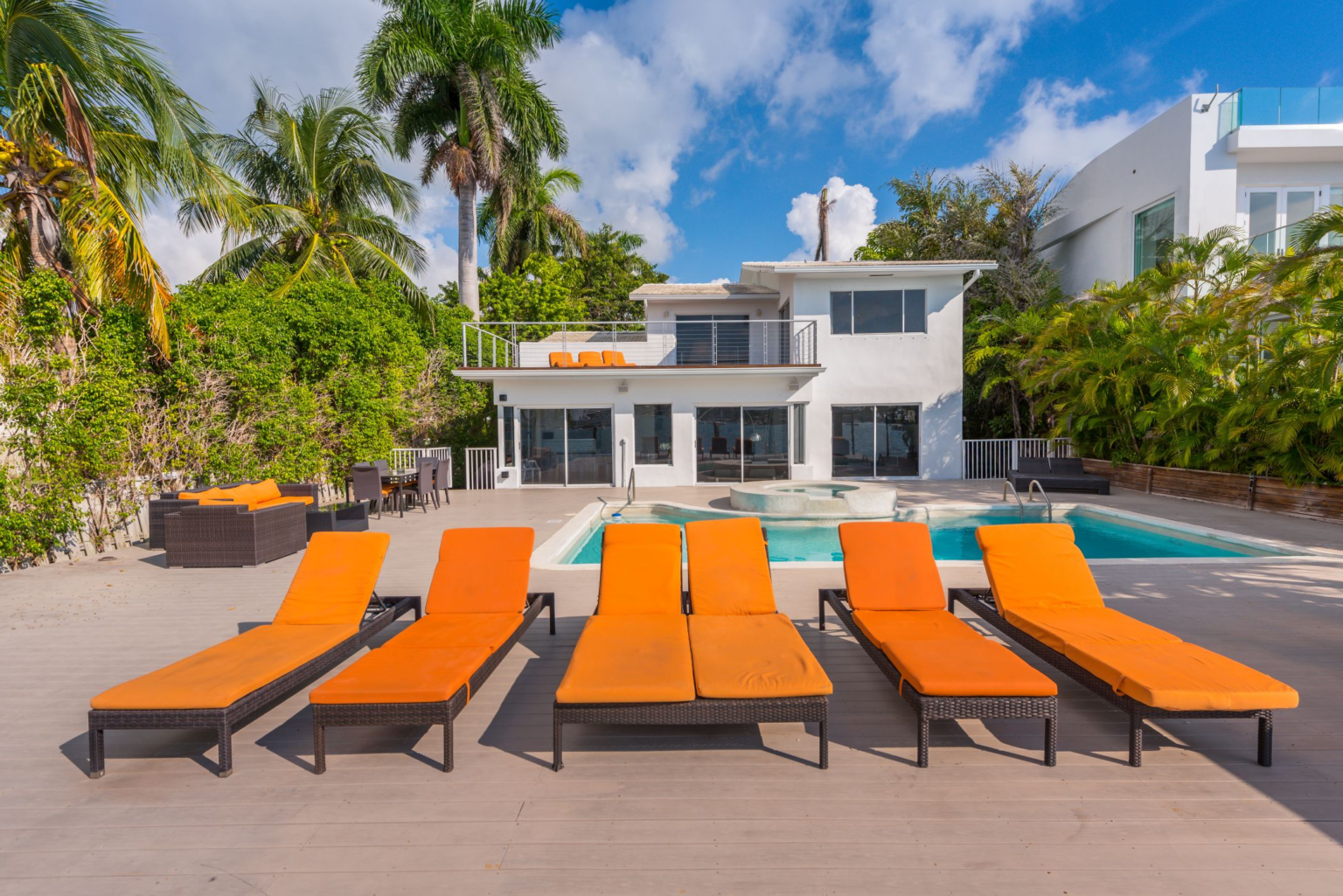 A row of orange lounge chairs are lined up in front of a large white house.