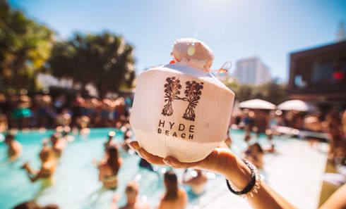 A person is holding a coconut in front of a swimming pool.