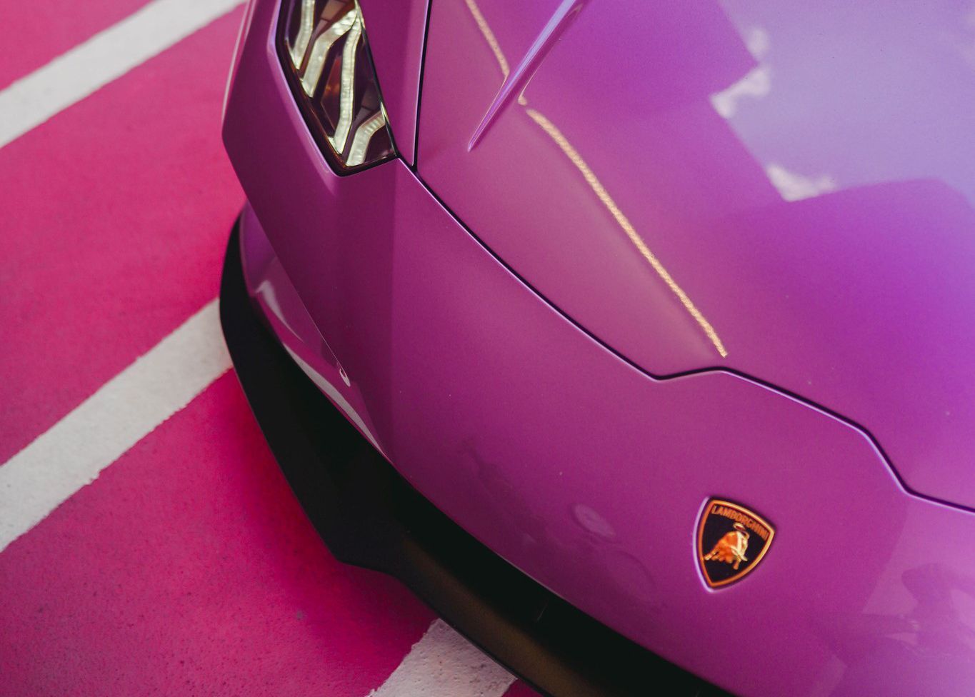 A purple Lamborghini is parked in a pink parking lot.