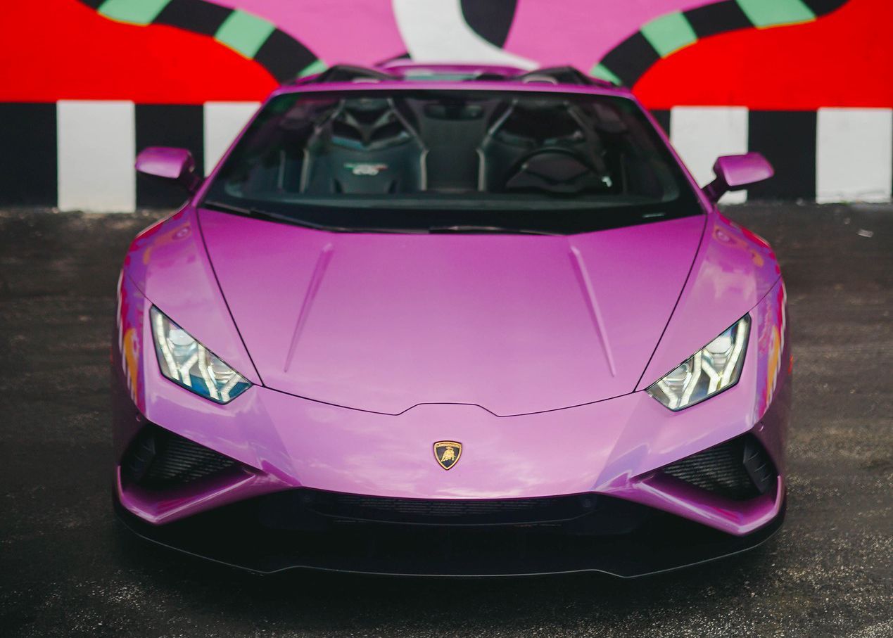A purple Lamborghini is parked in front of a checkered wall.