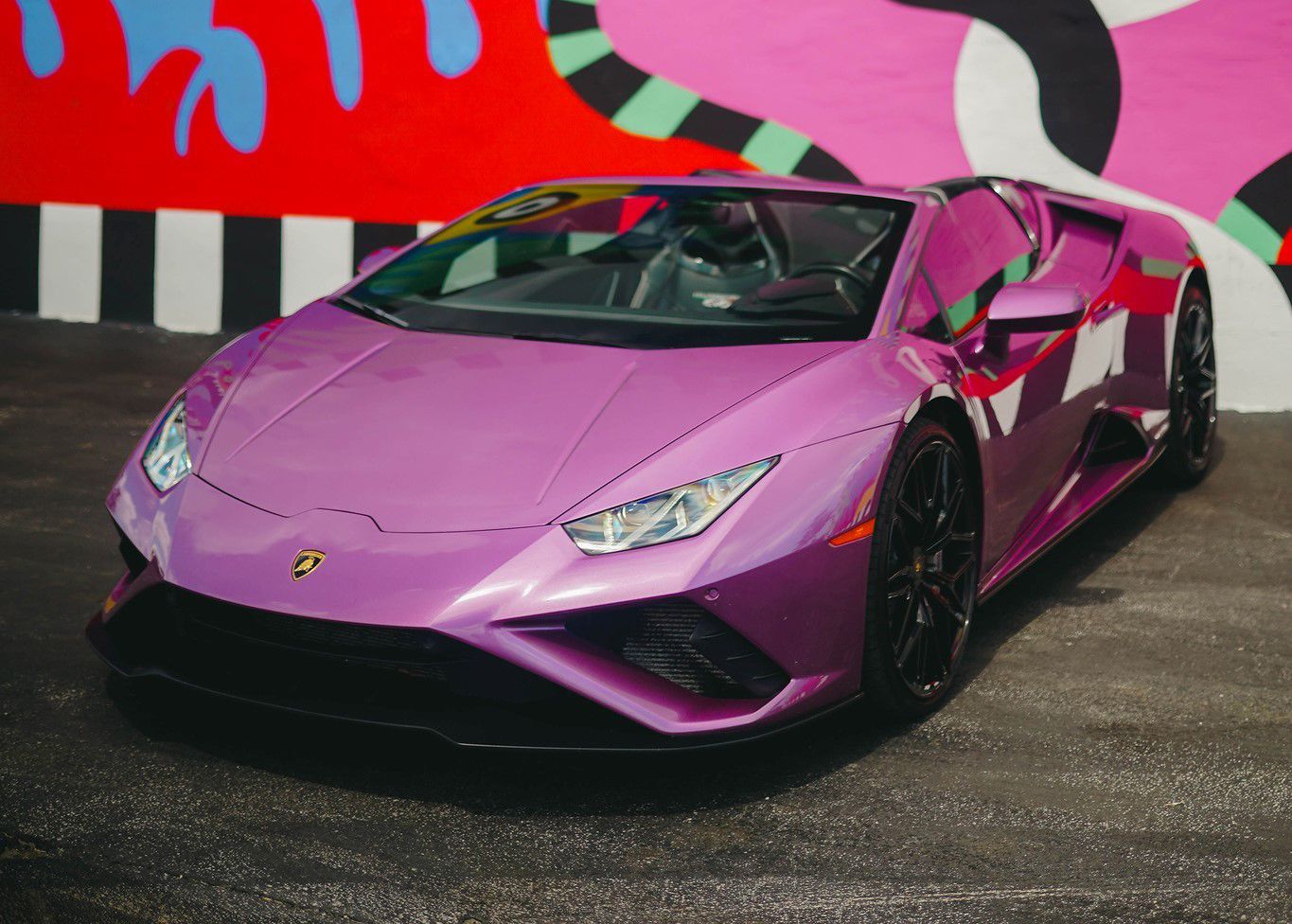 A purple Lamborghini is parked in front of a colorful wall.
