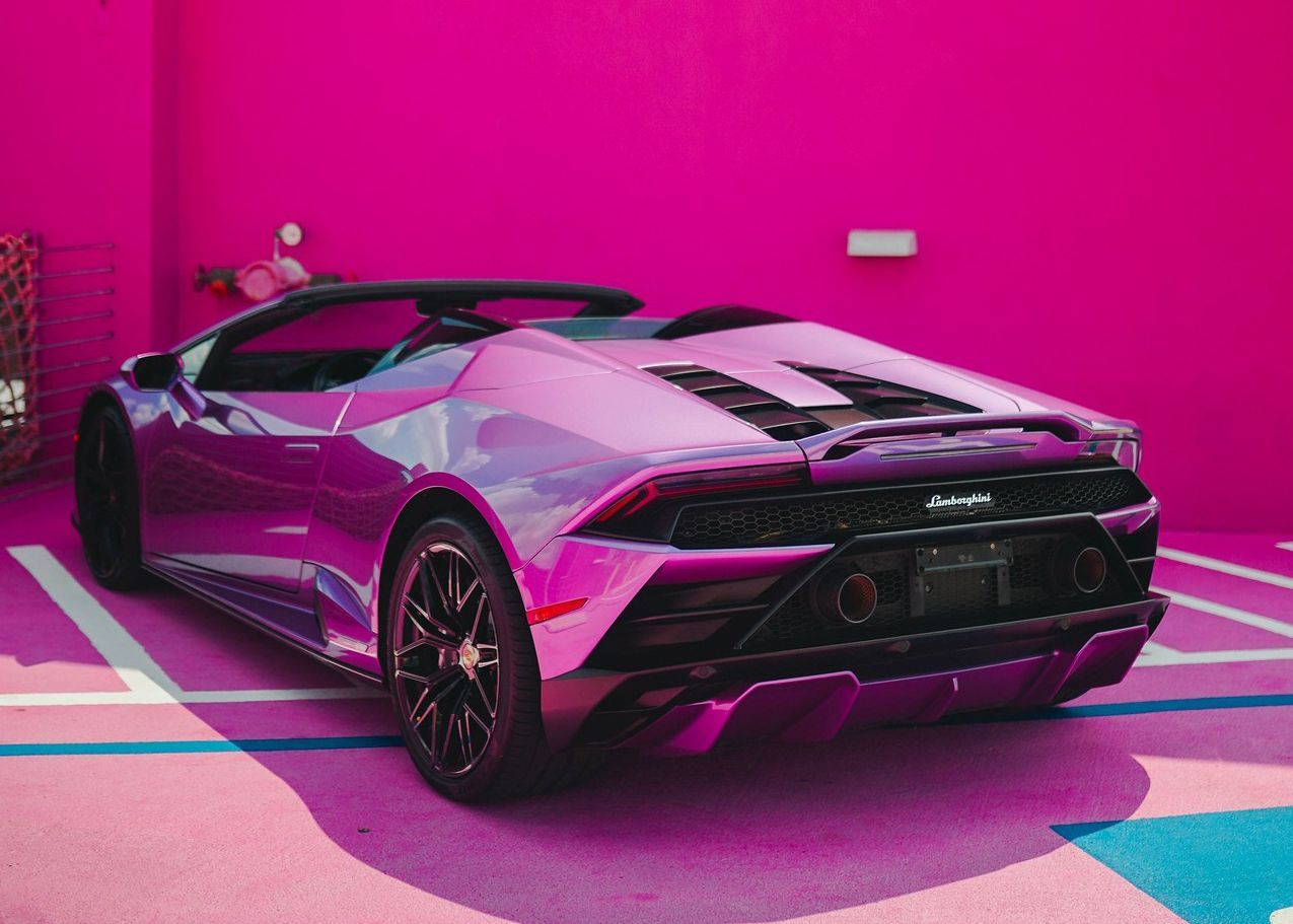 A purple sports car is parked in front of a pink wall.