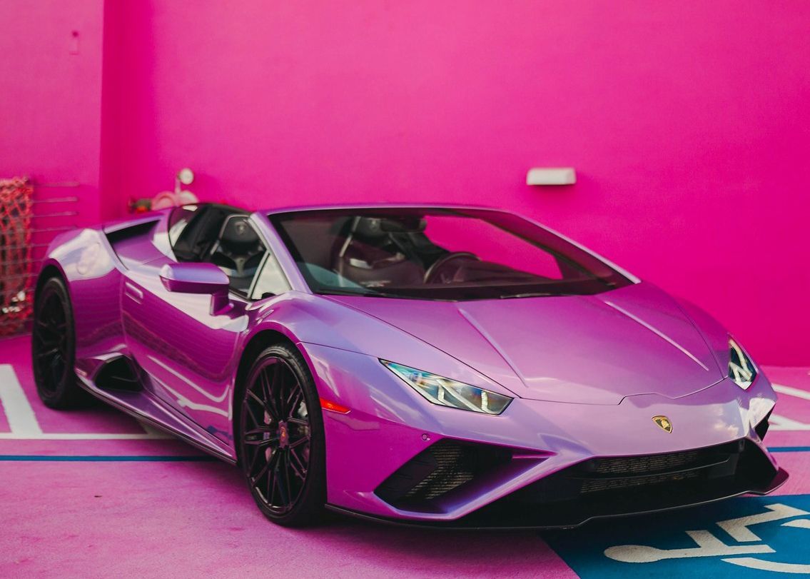 A purple Lamborghini Huracan is parked in front of a pink wall.