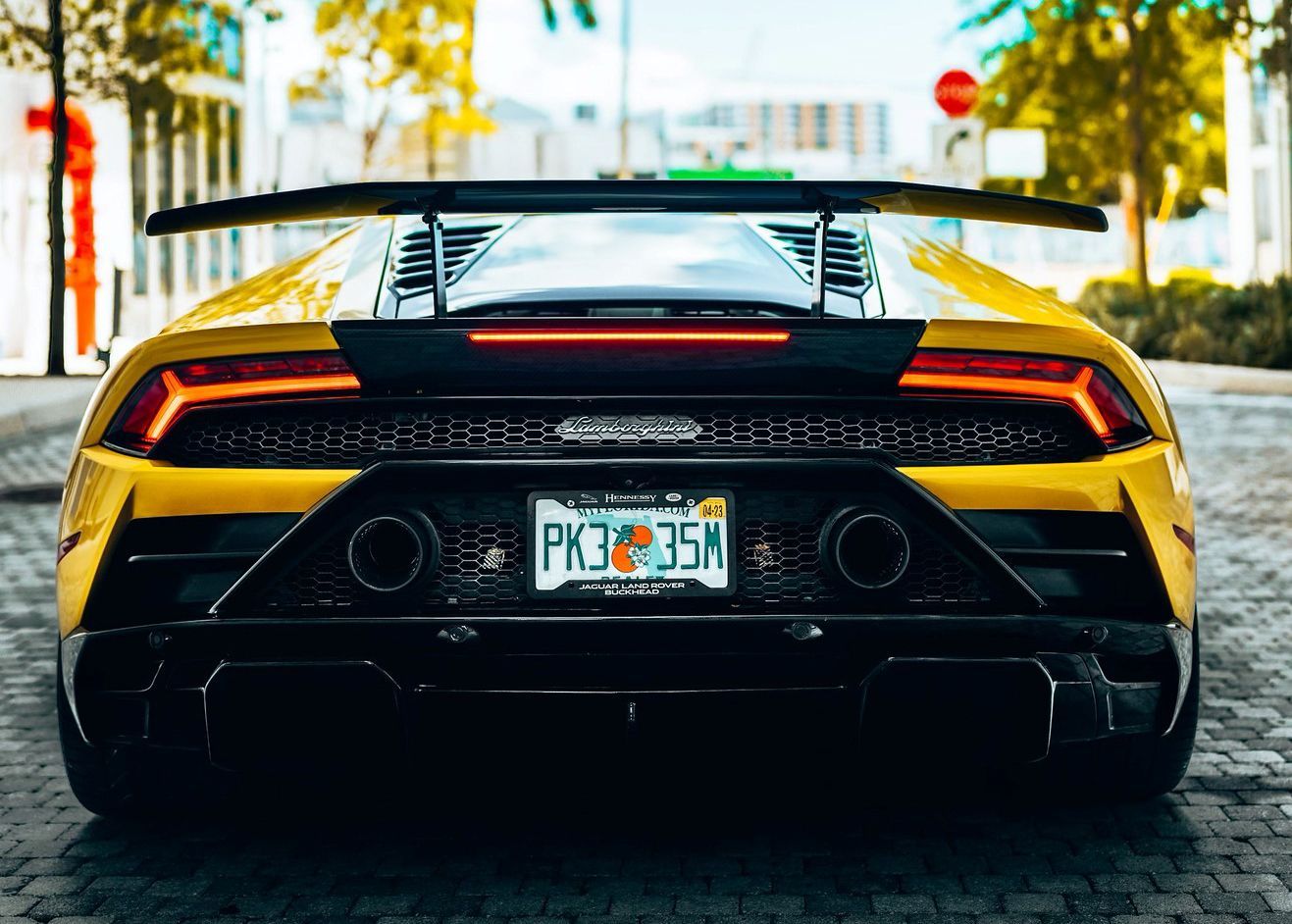 The back of a yellow Lamborghini Huracan is parked on a cobblestone street.