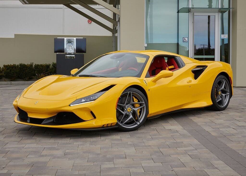 A yellow Ferrari F8 Spider is parked in front of a building.