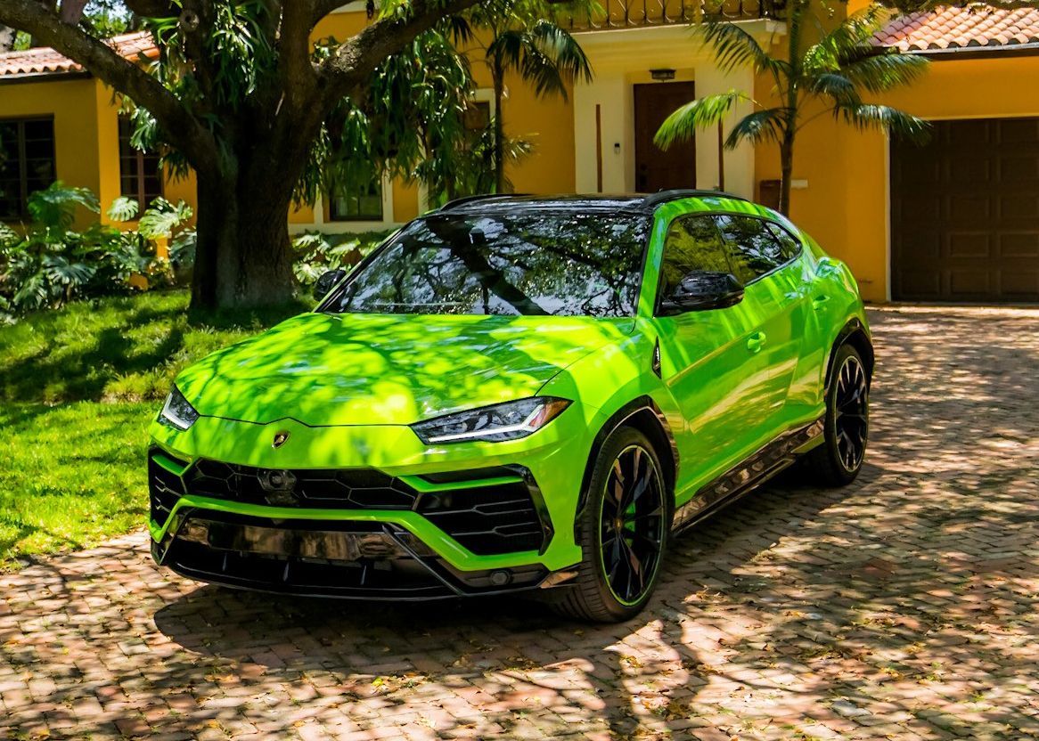 A green Lamborghini Urus is parked in front of a house.