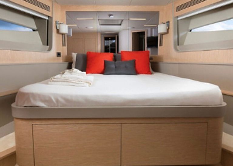 A bedroom on a boat with a bed and red pillows.