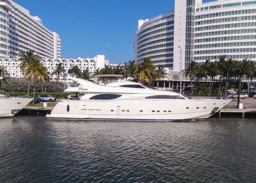 A large white yacht is docked in a harbor in front of a hotel.