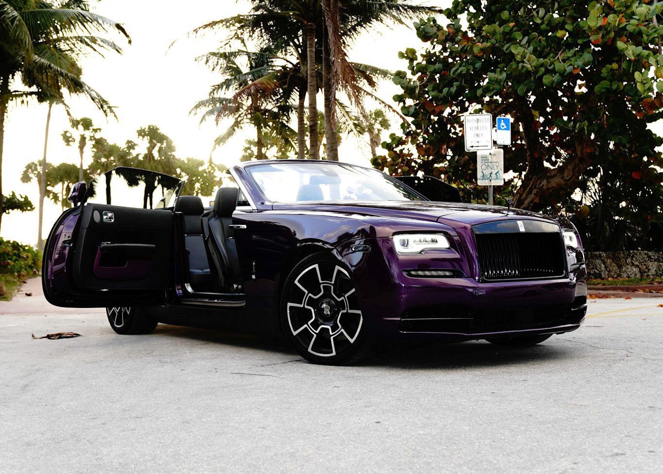 A purple car with the doors open is parked in a parking lot.