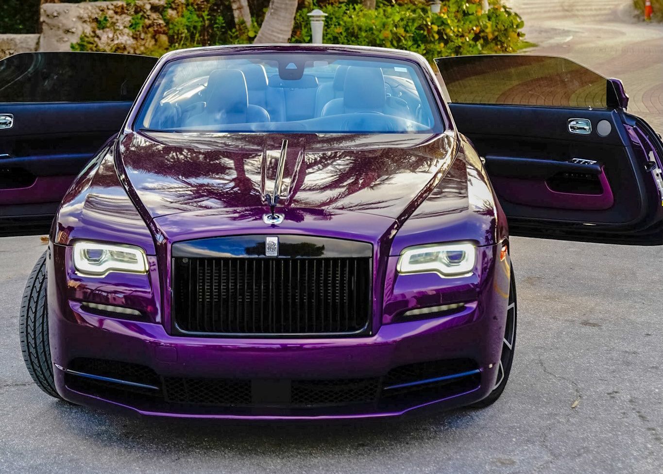 A purple Rolls Royce is parked in a driveway with its doors open.