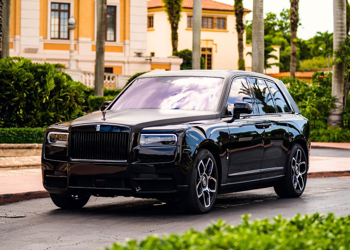 A black Rolls Royce Cullinan is parked on the side of the road in front of a building.