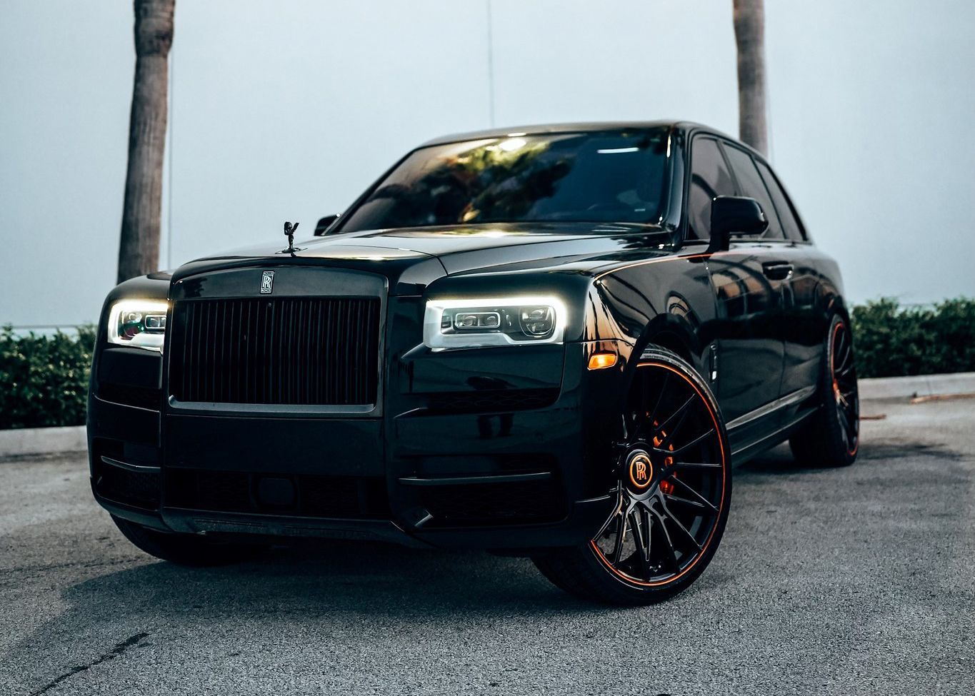 A black Rolls Royce is parked in a parking lot next to a palm tree.