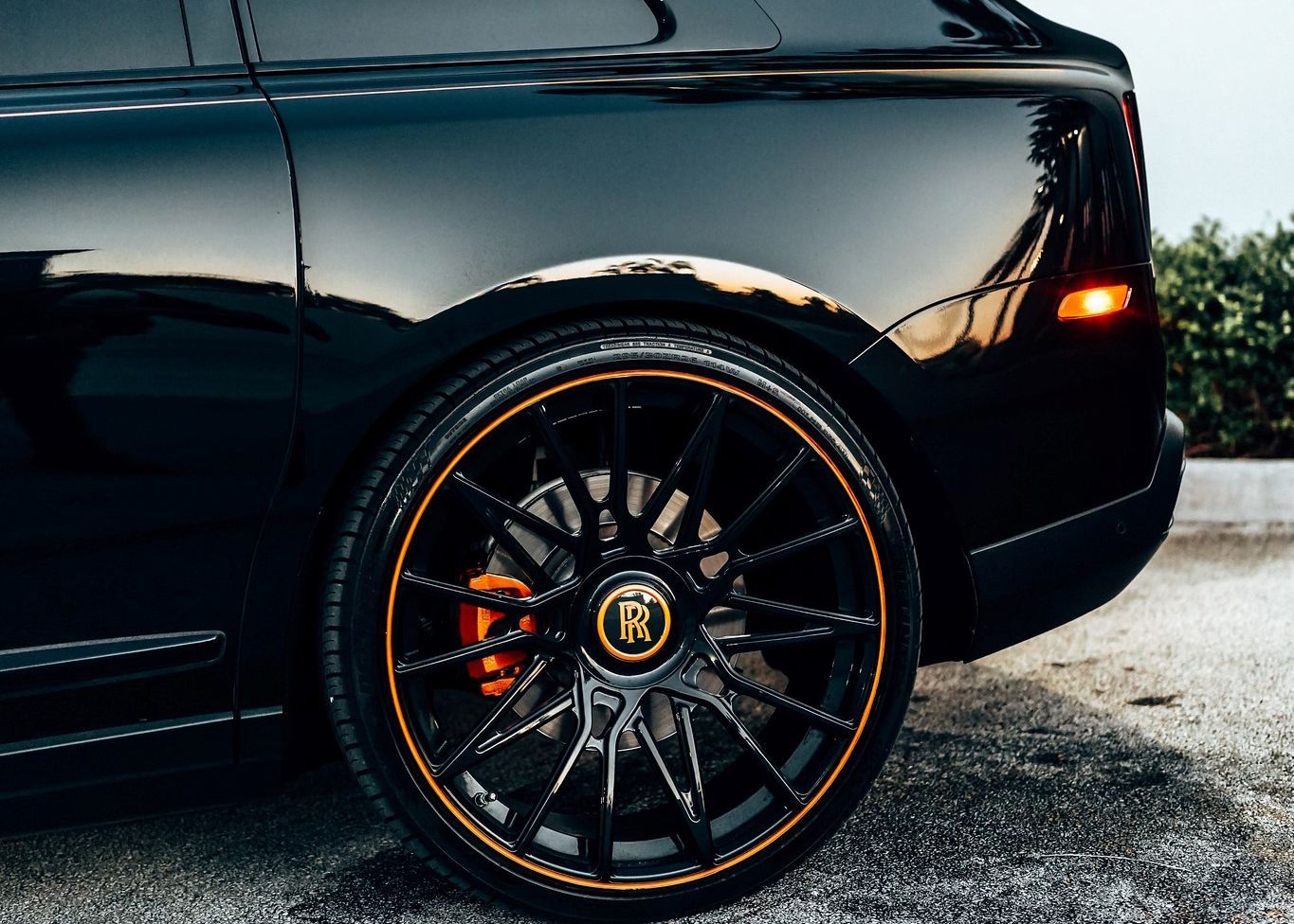 A black car with orange brake calipers is parked on the side of the road.