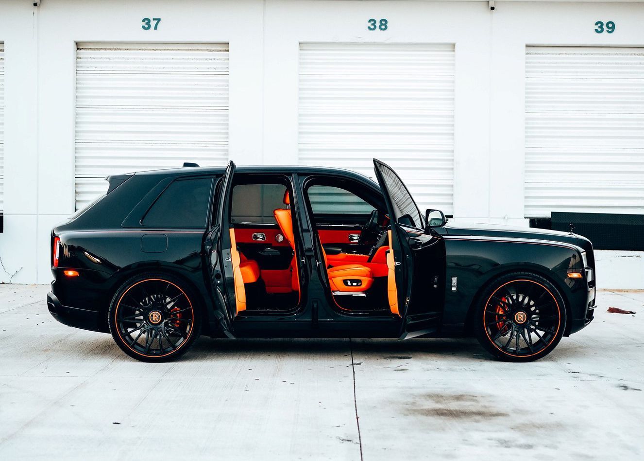 A black car with the doors open is parked in front of a garage.