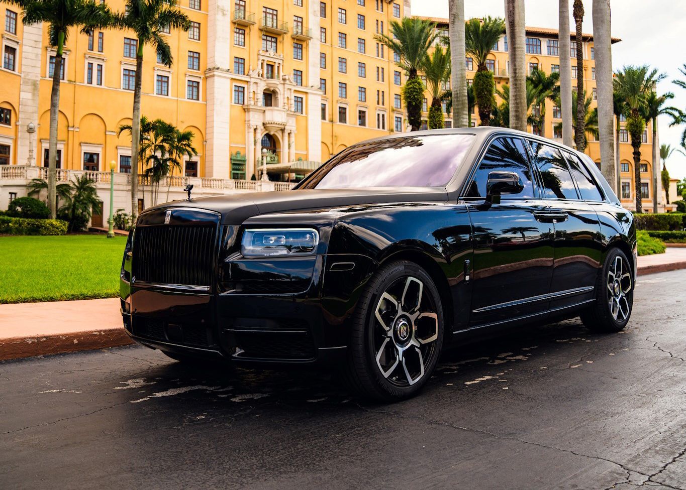A black Rolls Royce is parked on the side of the road in front of a building.