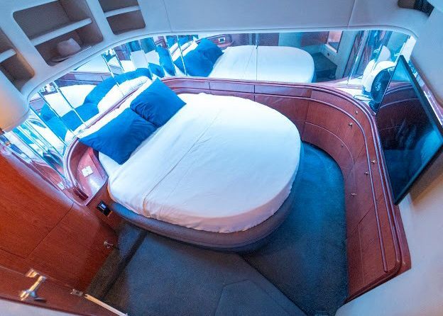 A bedroom on a boat with a round bed and blue pillows.