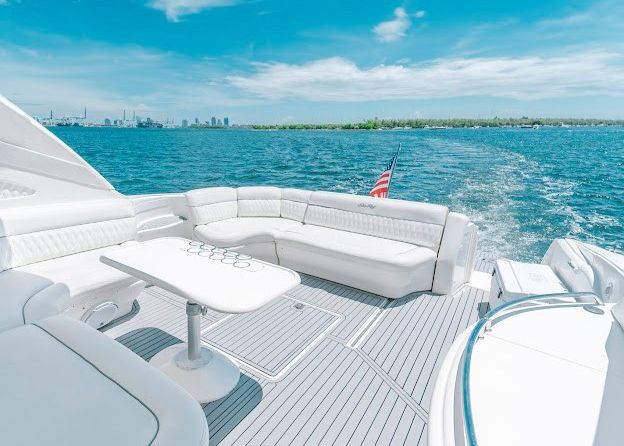 The back of a yacht with a table and couch is floating on top of a body of water.