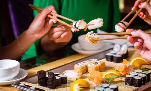 A group of people are eating sushi with chopsticks.