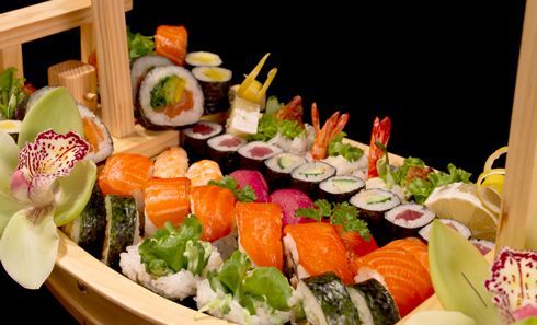 A wooden boat filled with sushi and flowers on a table.