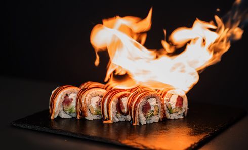 A row of sushi rolls on a black plate with flames coming out of them.