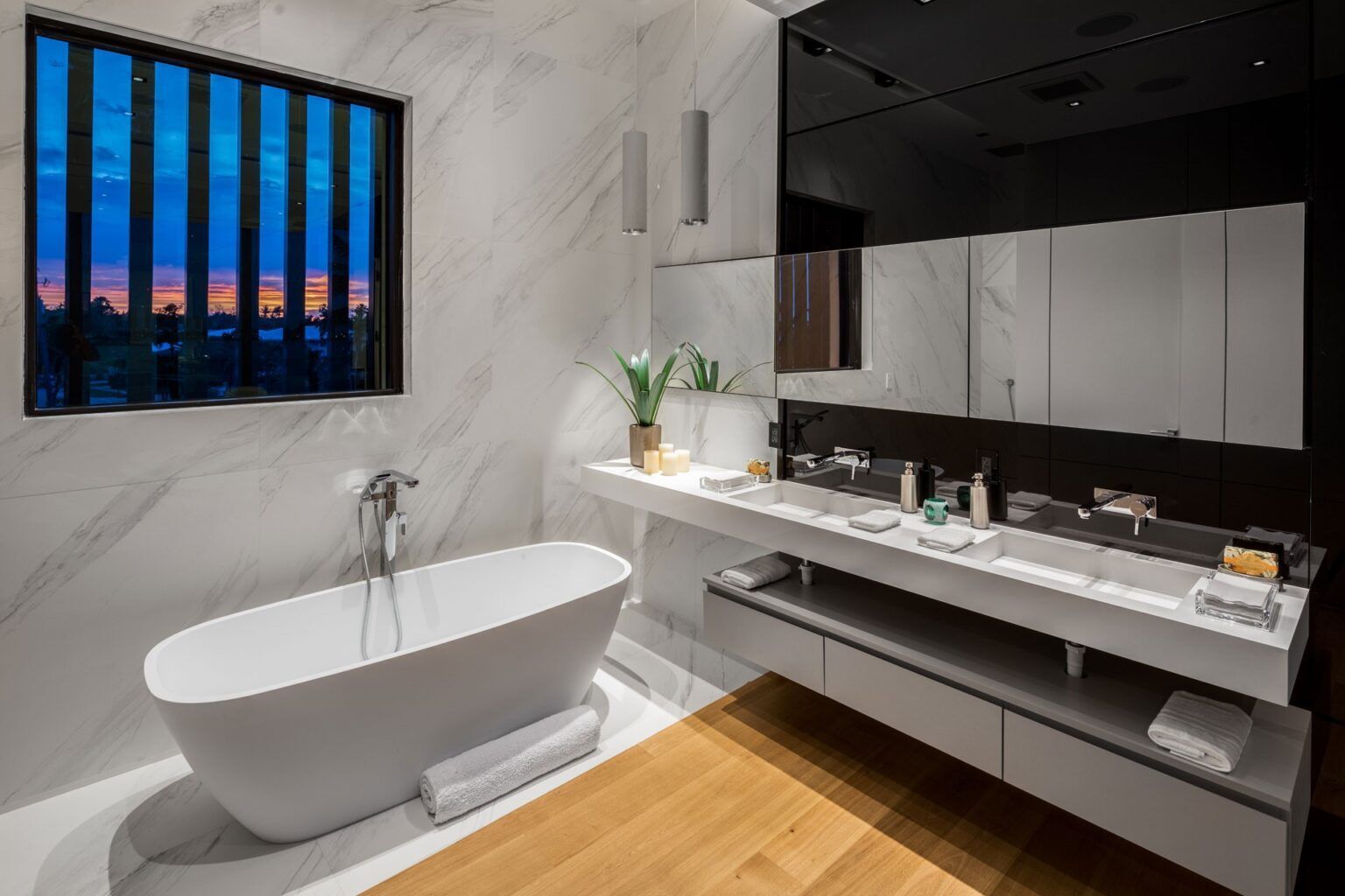 A bathroom with a tub, sink, mirror and window.