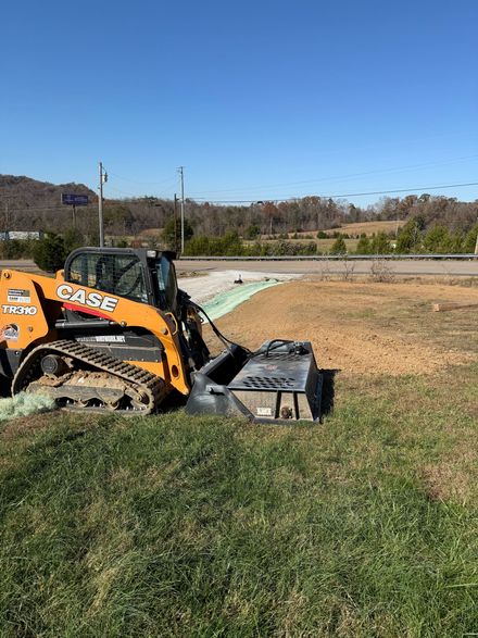 A yellow Case skid steer with a brush cutter attachment sits on a grassy field under a clear blue sky.