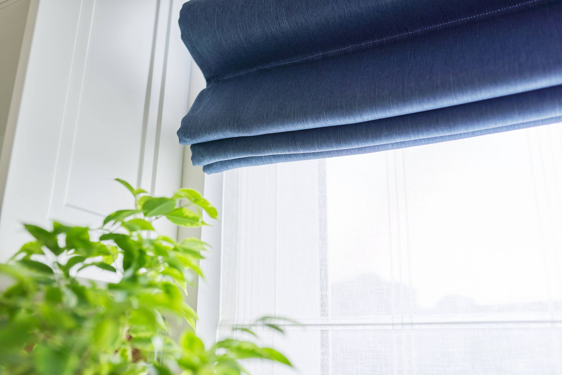 A blue roman shade covering a window next to a houseplant at Elden Draperies, Blinds and Shades near Toledo, OH