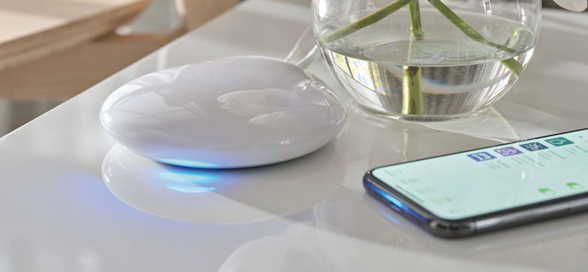 Hunter Douglas PowerView® Automation device on a counter beside smartphone.