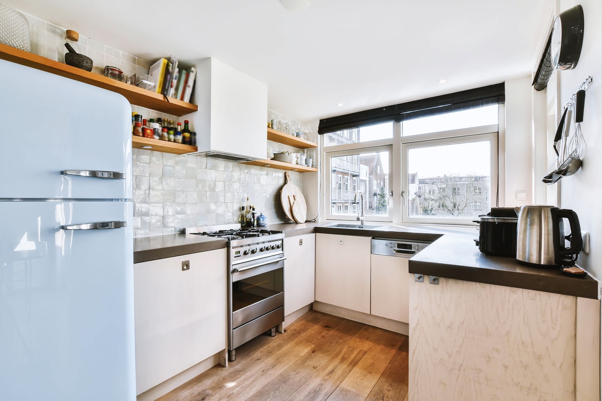  Small modern kitchen with two small windows covered by roller shades.