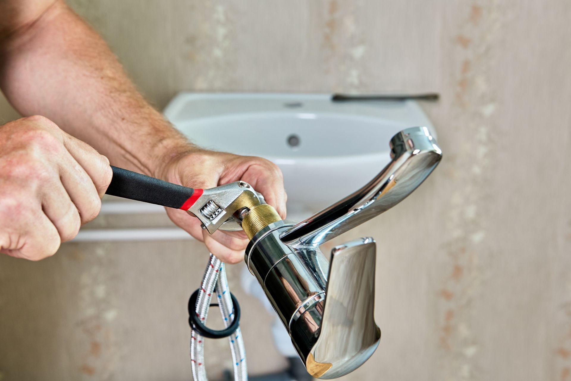 A man is fixing a faucet with a wrench in a bathroom.