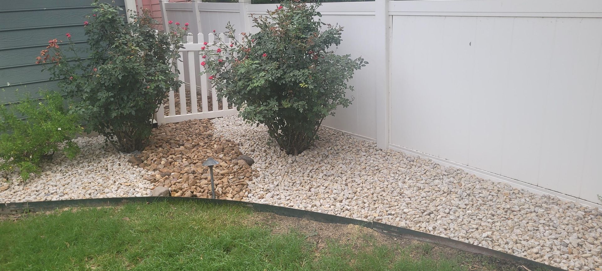 A white fence is surrounded by gravel and shrubs in a yard.