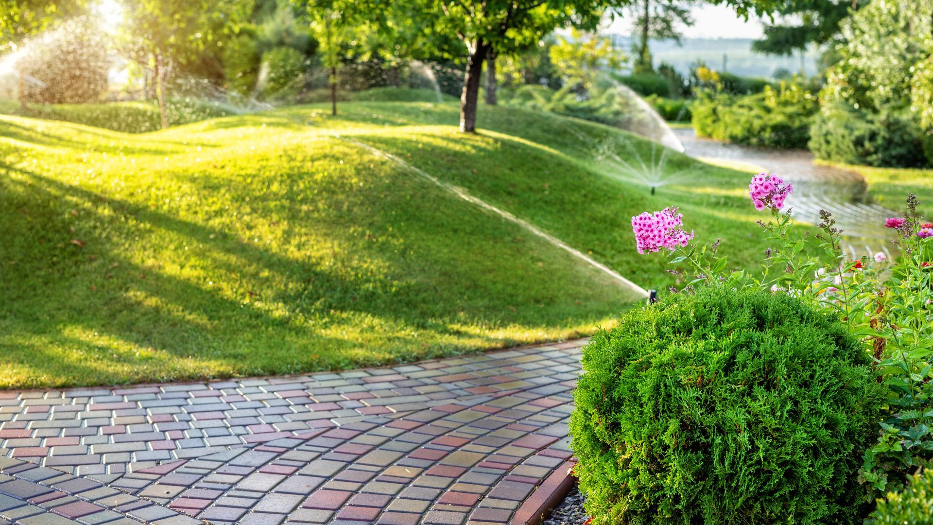 A sprinkler is spraying water on a lush green lawn in a park.