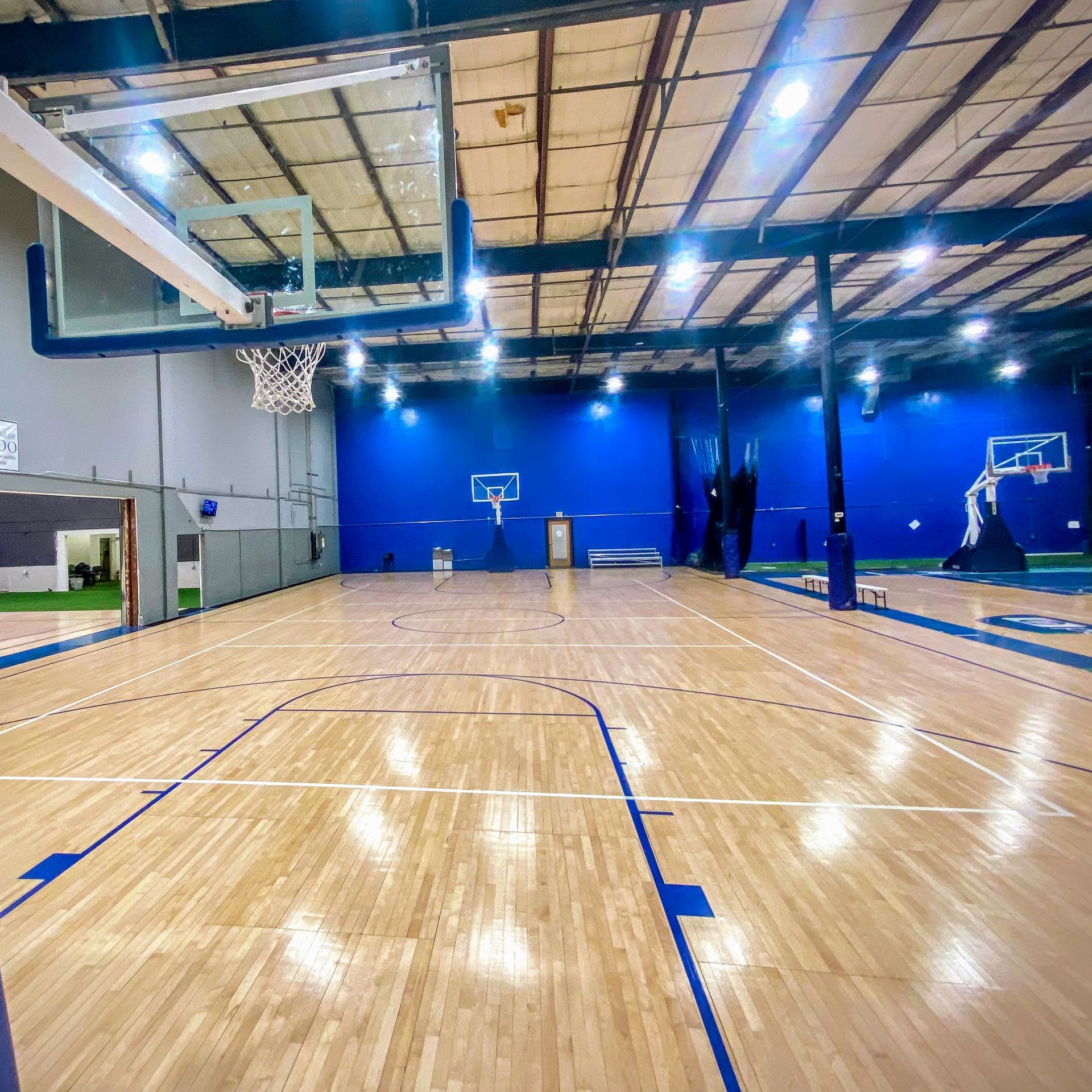 Basketball court with wooden floor, blue walls, and multiple hoops.