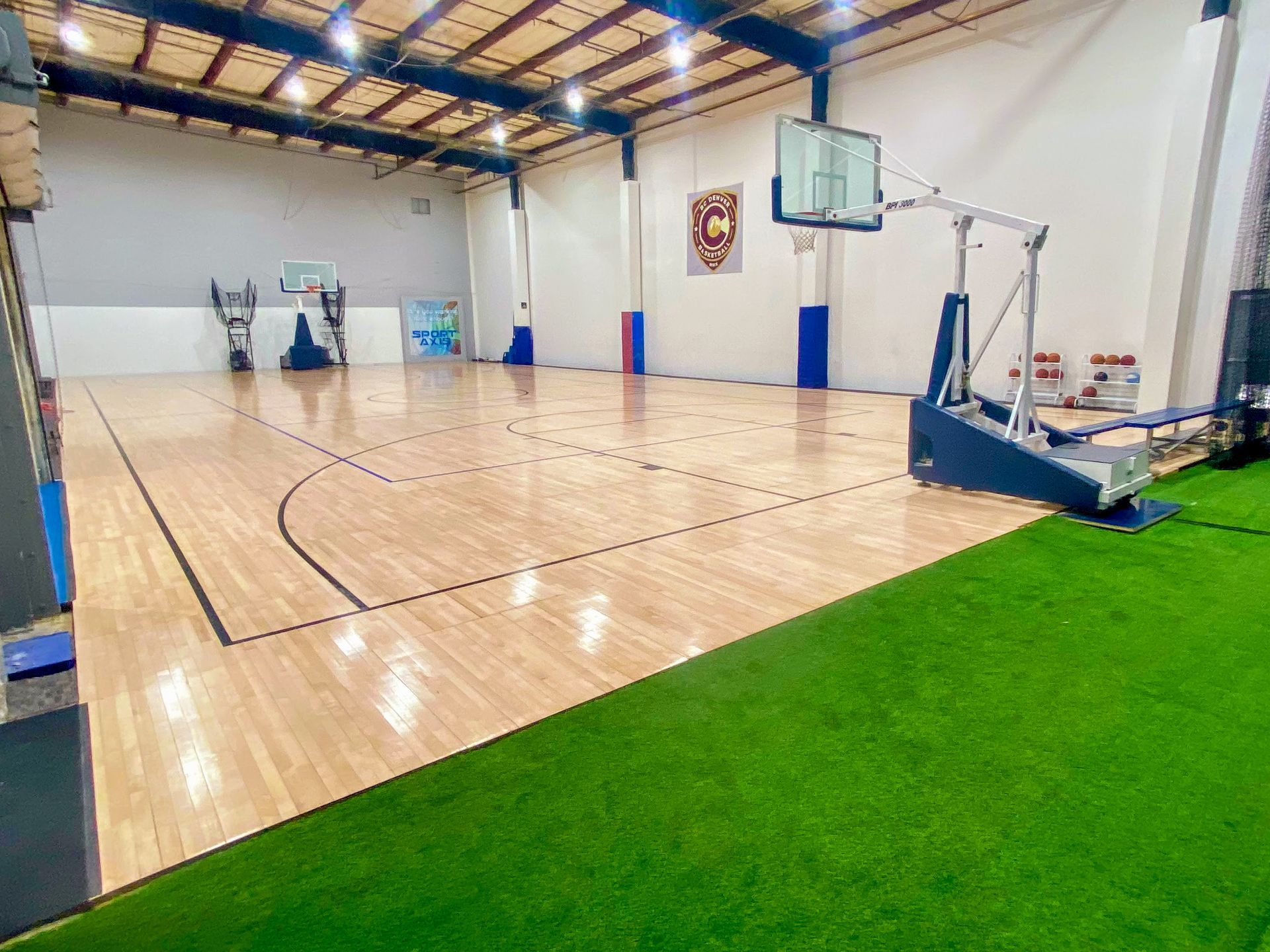 Basketball court with wooden floor, artificial turf, hoops, and a logo on the wall.