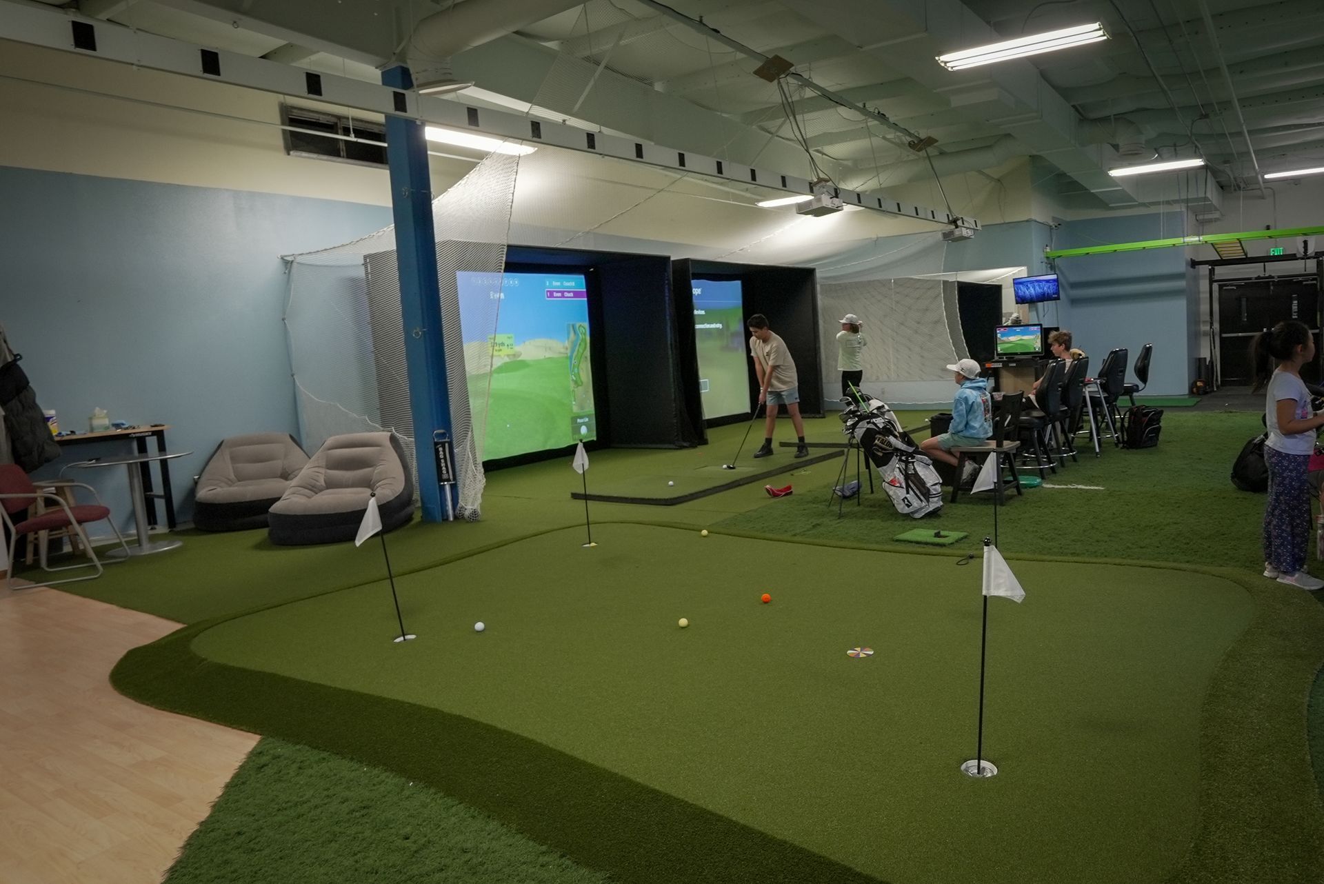 Indoor golf facility with putting green, simulators, and people playing.
