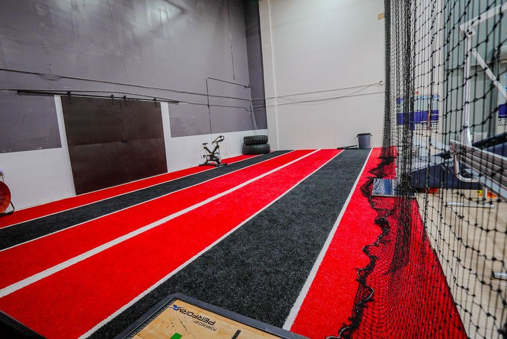 Indoor athletic track with red and black lanes, enclosed by a net.