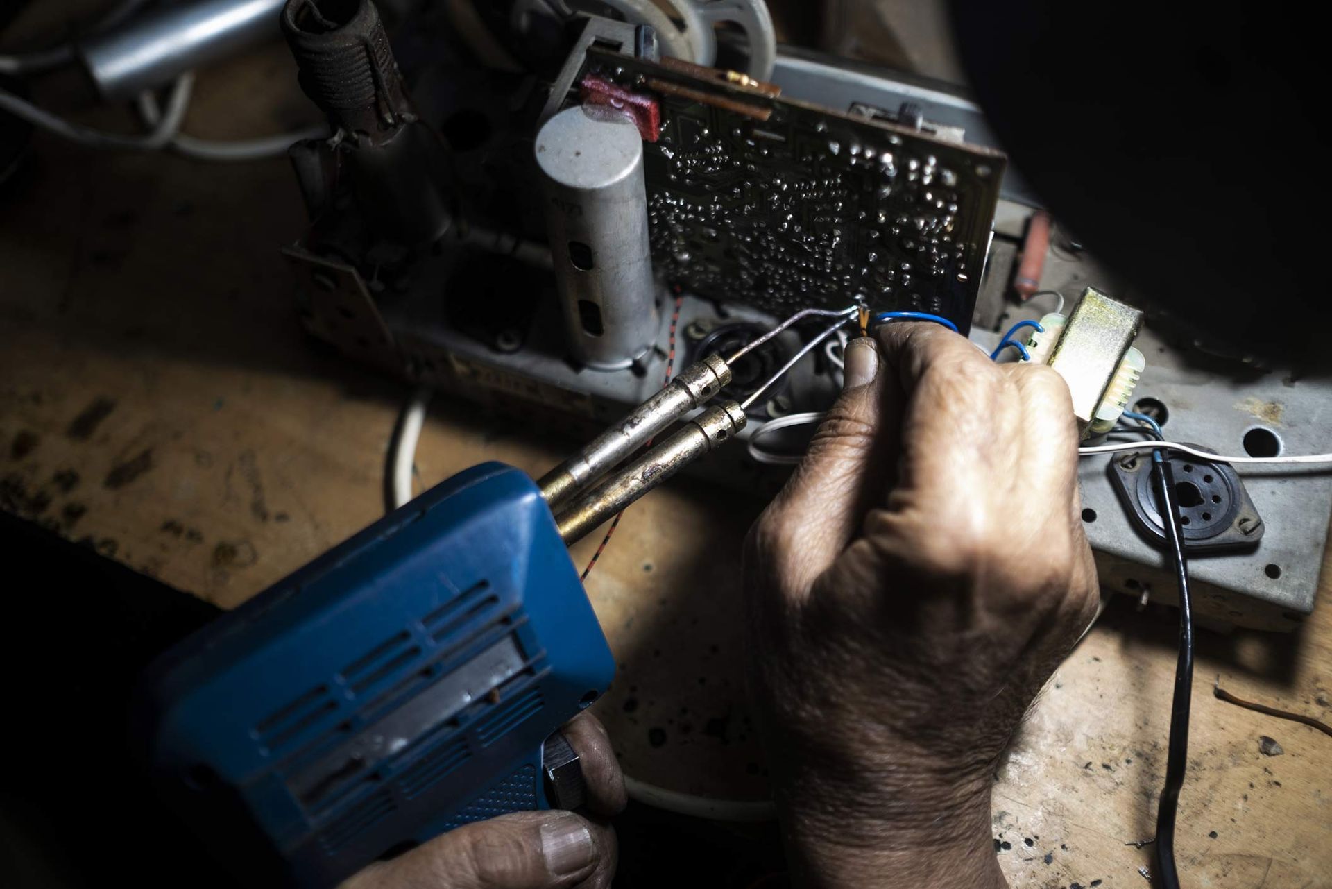Person soldering circuit board with a blue soldering iron on a workbench.