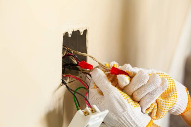 Hands wearing work gloves connecting electrical wires inside a wall outlet.