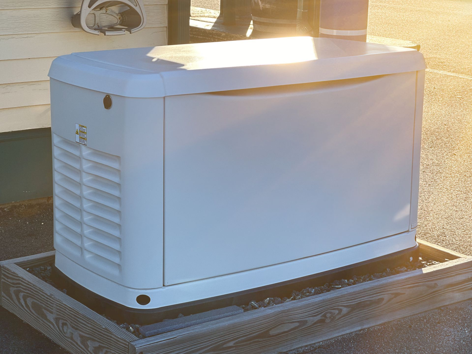 A white generator sits on a wooden base outdoors, with a slatted side and a person visible behind it.