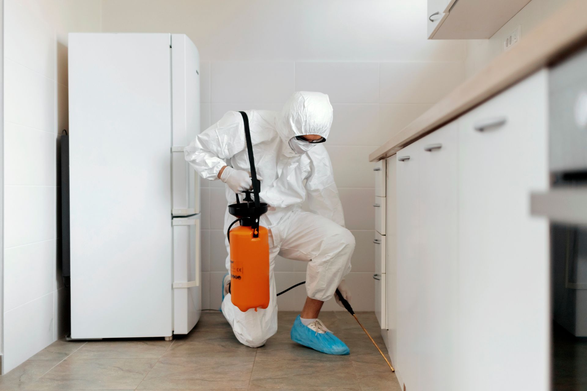 Pest control worker in protective gear performing termite treatment in a residential kitchen.