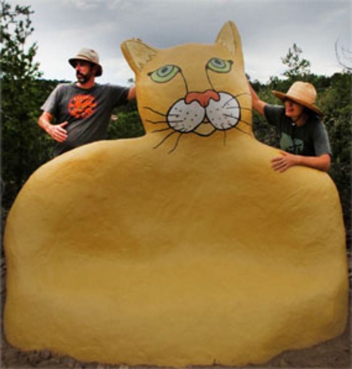two people standing next to a large yellow cat statue