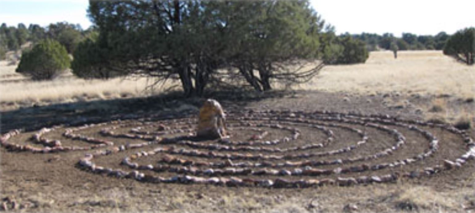 a labyrinth made of rocks in a field with trees in the background .